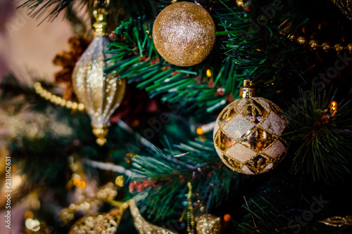 Fir branch with balls and festive lights on the Christmas background with sparkles.Golden Ball with Glitter as Decorative Christmas Ornament on a Artificial Tree.New year decoration.Selective focus