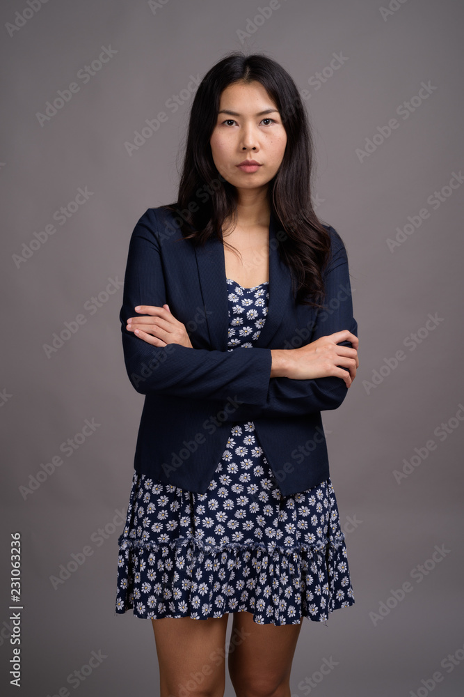 Asian woman wearing blue dress and cardigan sweater against gray Asian woman wearing blue dress and cardigan sweater against gray