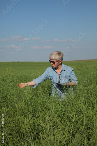 Female agronomist or farmer examining green canola field  rapeseed plant in spring using tablet