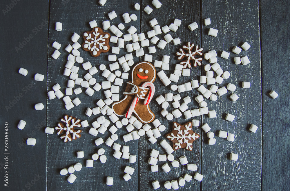 Gingerbread men with candy cane snowflakes and marshmallows laying on grey wood background. Christmas or New Year composition. Christmas card.
