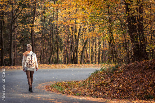 Woman walking on the road in the middle of forest at autumn season
