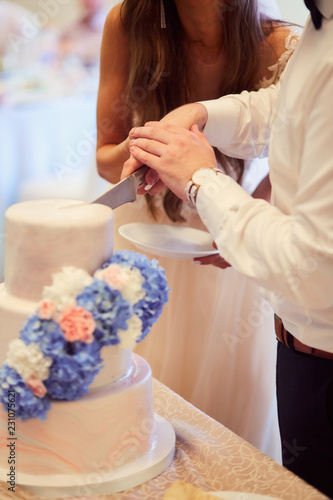 Bride and groom cut white layered wedding cake decorated with blue and white hydrangeas