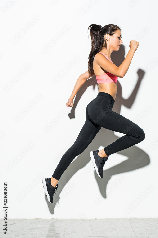 Attractive excited fitness girl in sportwear jumping isolated over white background