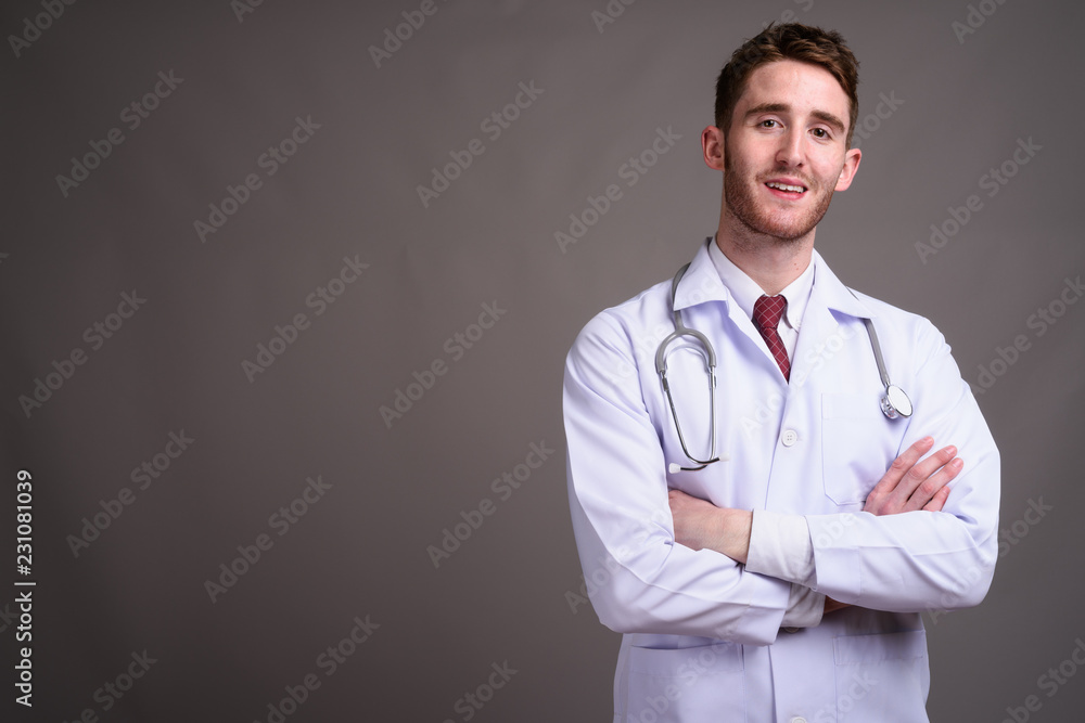 Young handsome man doctor against gray background Young handsome man doctor against gray background