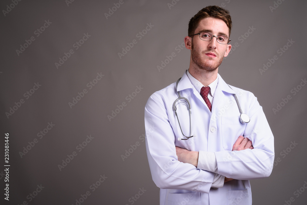 Young handsome man doctor wearing eyeglasses against gray backgr Young handsome man doctor wearing eyeglasses against gray backgr