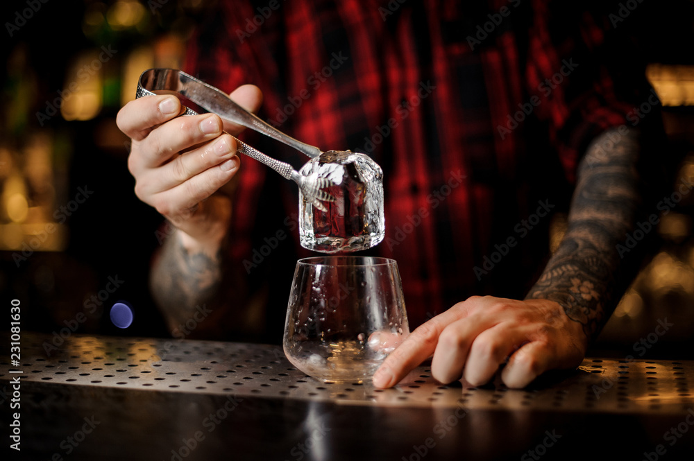 Bartender putting an ice cube to a glass preparing a James Cook cocktail
