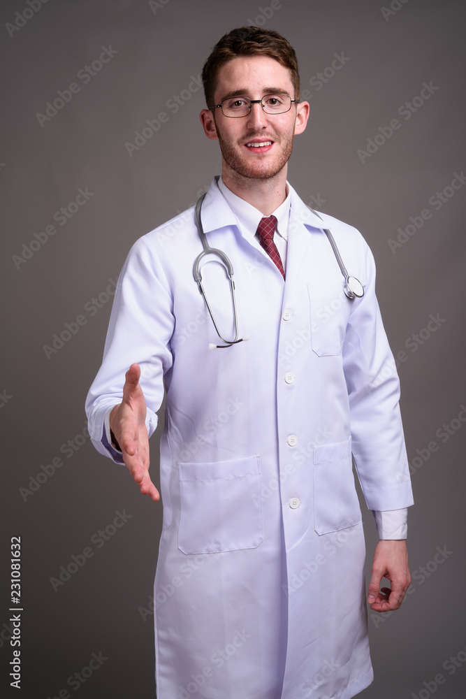 Young handsome man doctor wearing eyeglasses against gray backgr Young handsome man doctor wearing eyeglasses against gray backgr