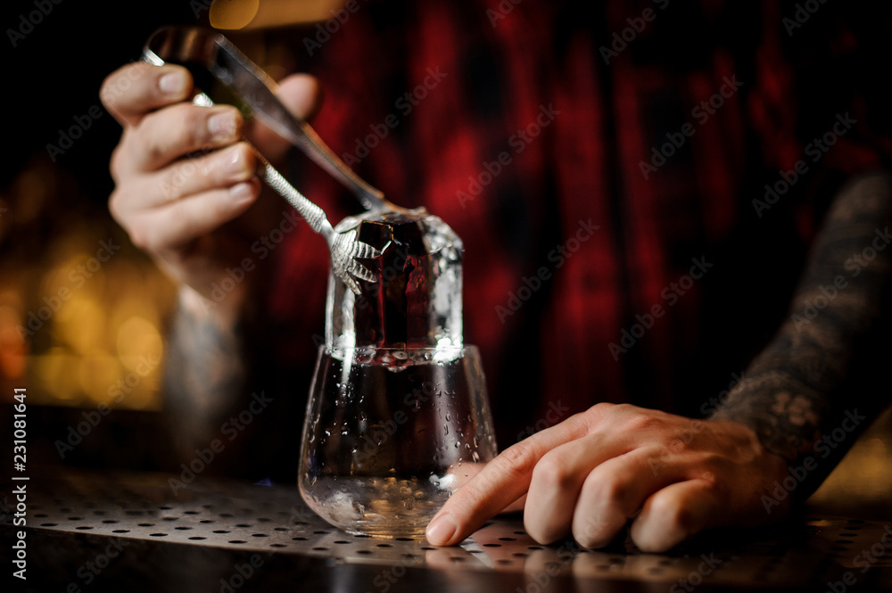 Bartender putting a big ice cube to a glass preparing a James Cook cocktail