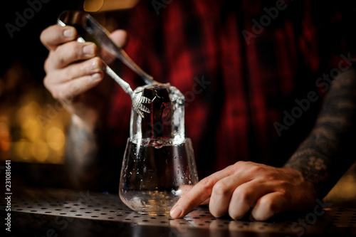 Bartender putting a big ice cube to a glass preparing a James Cook cocktail