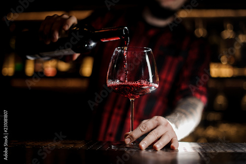 Professional bartender pourring a delicious wine from a bottle to a glass
