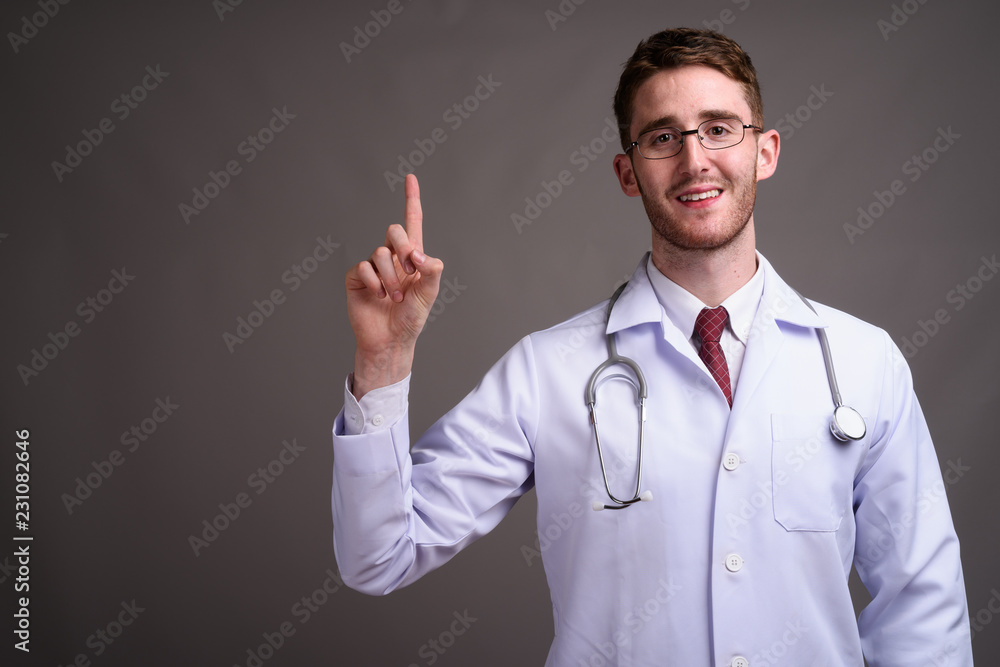 Young handsome man doctor wearing eyeglasses against gray backgr Young handsome man doctor wearing eyeglasses against gray backgr