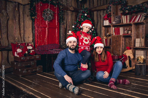 Happy family in Christmas hats sitting in a room in a rustic style. Daughter raises hats to parents.