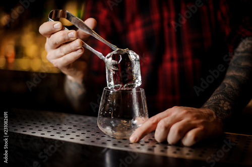 Bartender hand putting a big ice cube into a whiskey dof