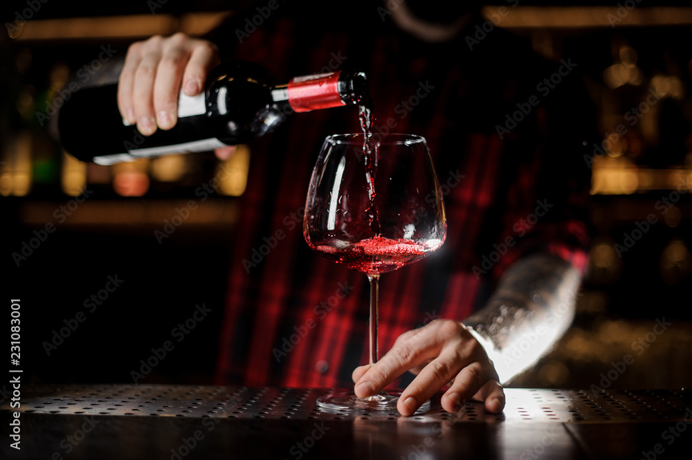 Tattooed barman pouring red wine into the burgunya glass