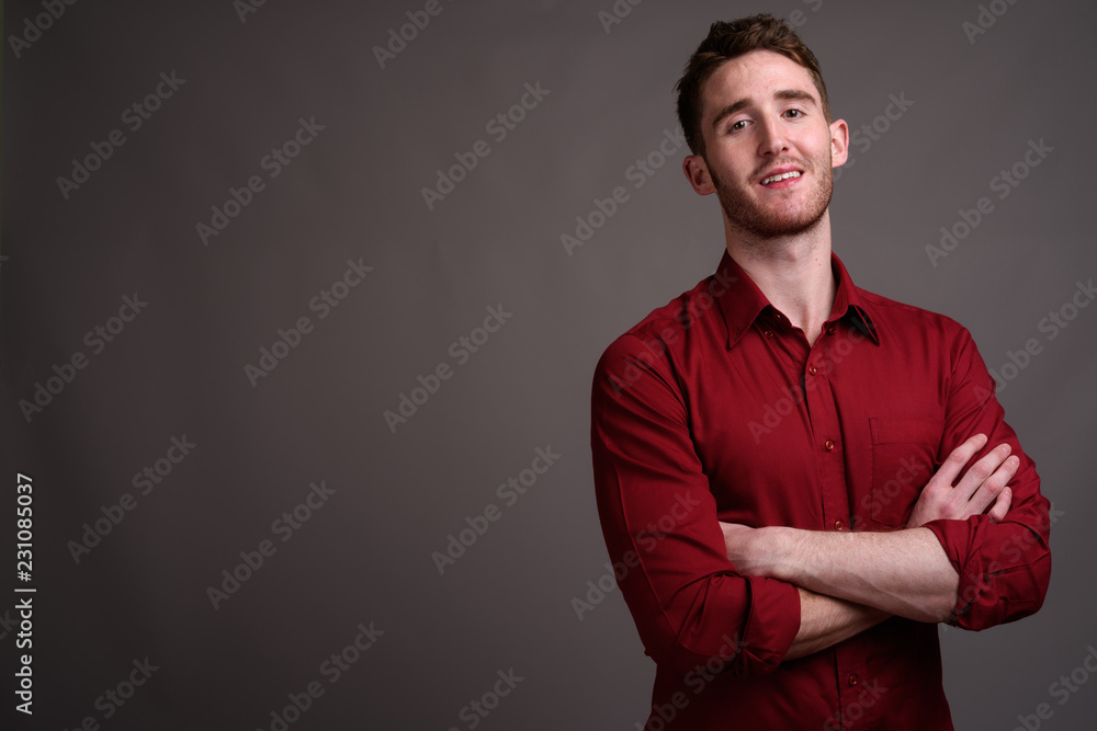 Young handsome businessman wearing red shirt against gray backgr Young handsome businessman wearing red shirt against gray backgr