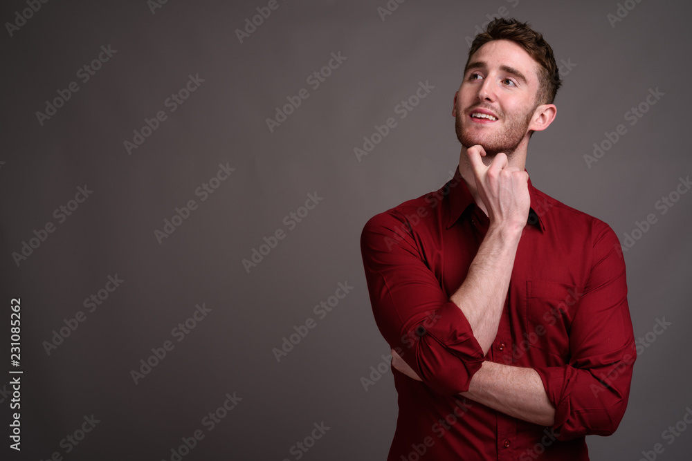 Young handsome businessman wearing red shirt against gray backgr