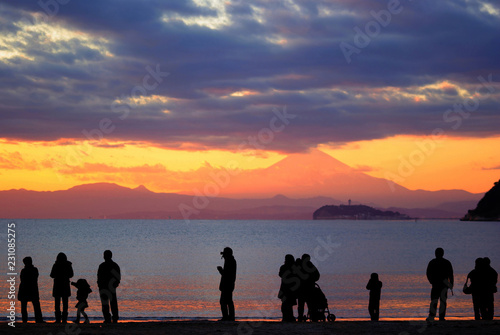 海岸で富士山が見える美しい夕景を眺めるシルエットの人々