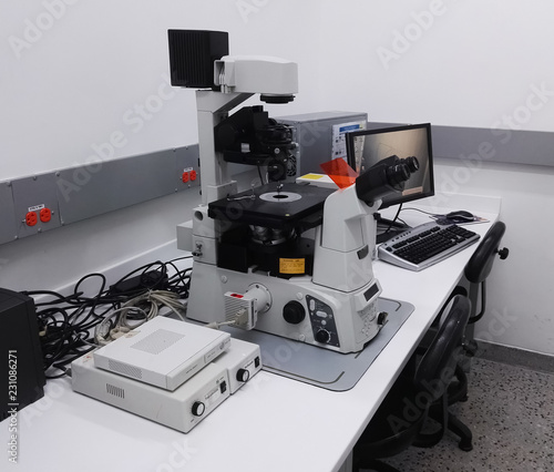 Desk with a high-tech microscopy station in a scientific laboratory. High magnification inverted fluorescence microscope, computer, electrical equipment and cables. photo