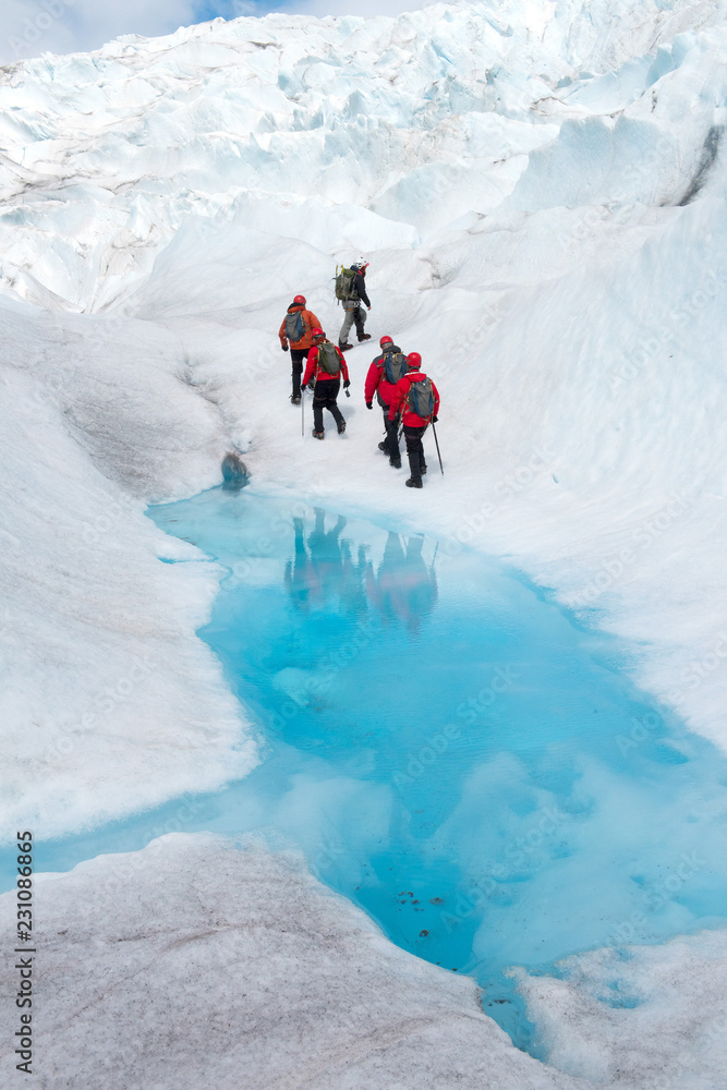 Hikers walk by colorful blue meltwater on a glacier in Alaska