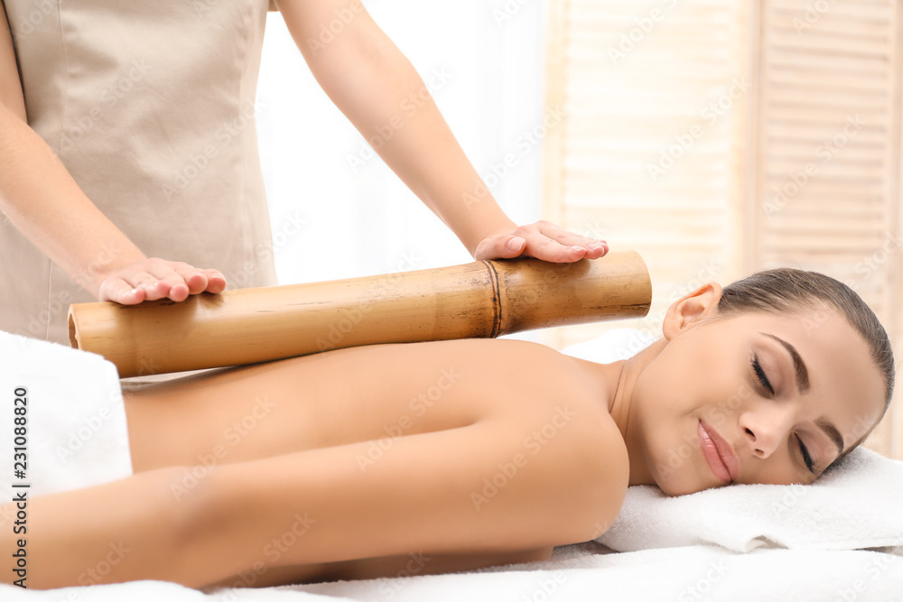 Obraz premium Young woman having massage with bamboo stick in wellness center