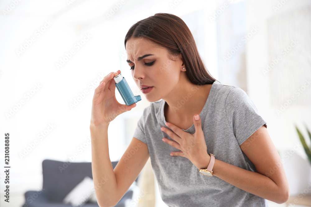 Young woman with asthma inhaler in light room - obrazy, fototapety, plakaty 