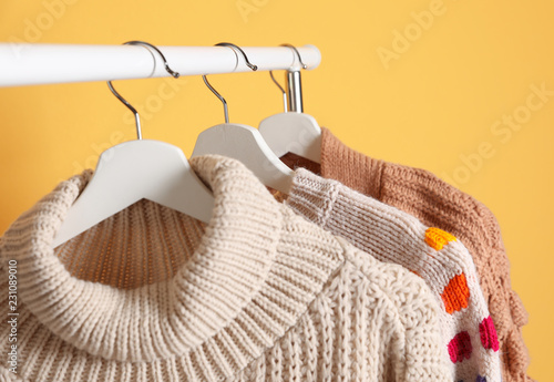 Collection of warm sweaters hanging on rack against color background, closeup