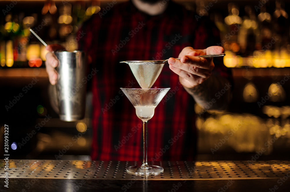 Bartender holding a steeel cocktail shaker and sieve above the glass