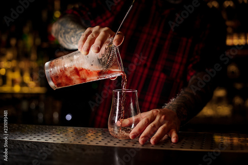 Bartender pourring a red Sazerac cocktail from the measuring cup