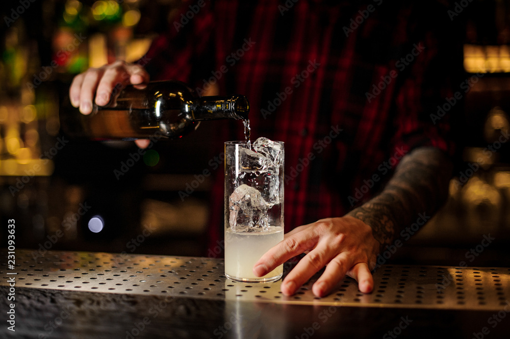 Bartender pourring a achohol from the bottle making cocktail