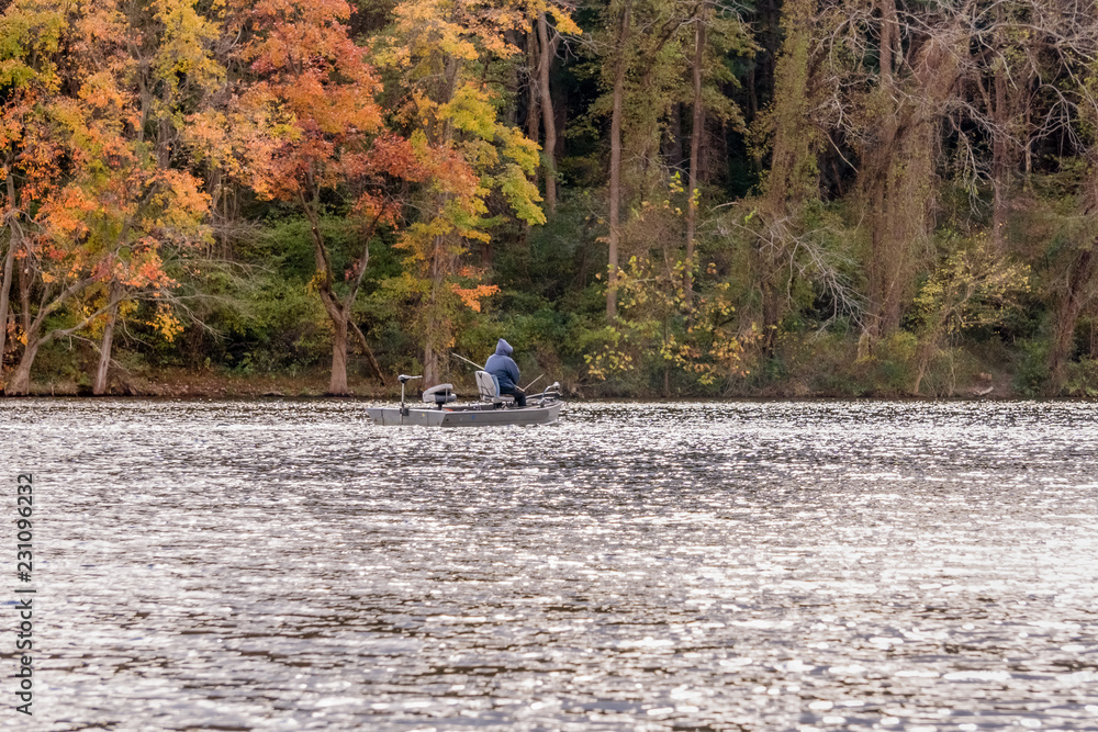 man in a boat fishing in a forest lake against red autumn foliage