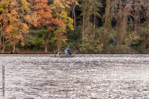 man in a boat fishing in a forest lake against red autumn foliage