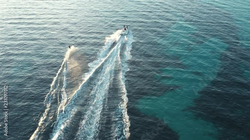 Video from above, aerial view of a person who is doing water skiing at sunset. Sardinia, Italy. photo