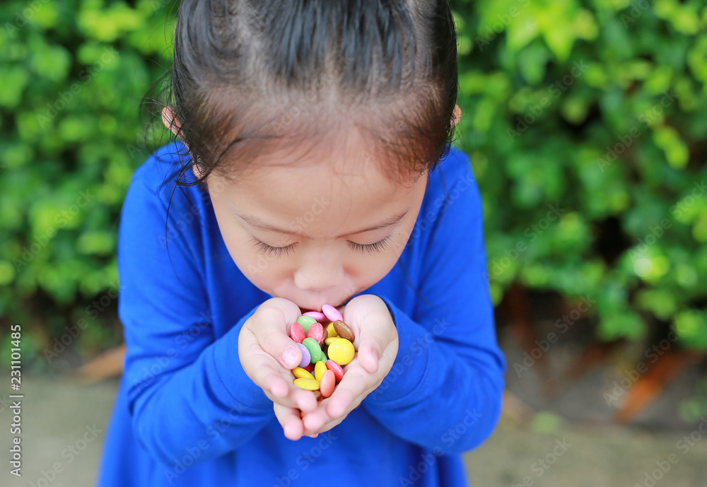Close-up little Asian child girl holding some colored coated chocolate candy in her hands. Close-up little Asian child girl holding some colored coated chocolate candy in her hands.