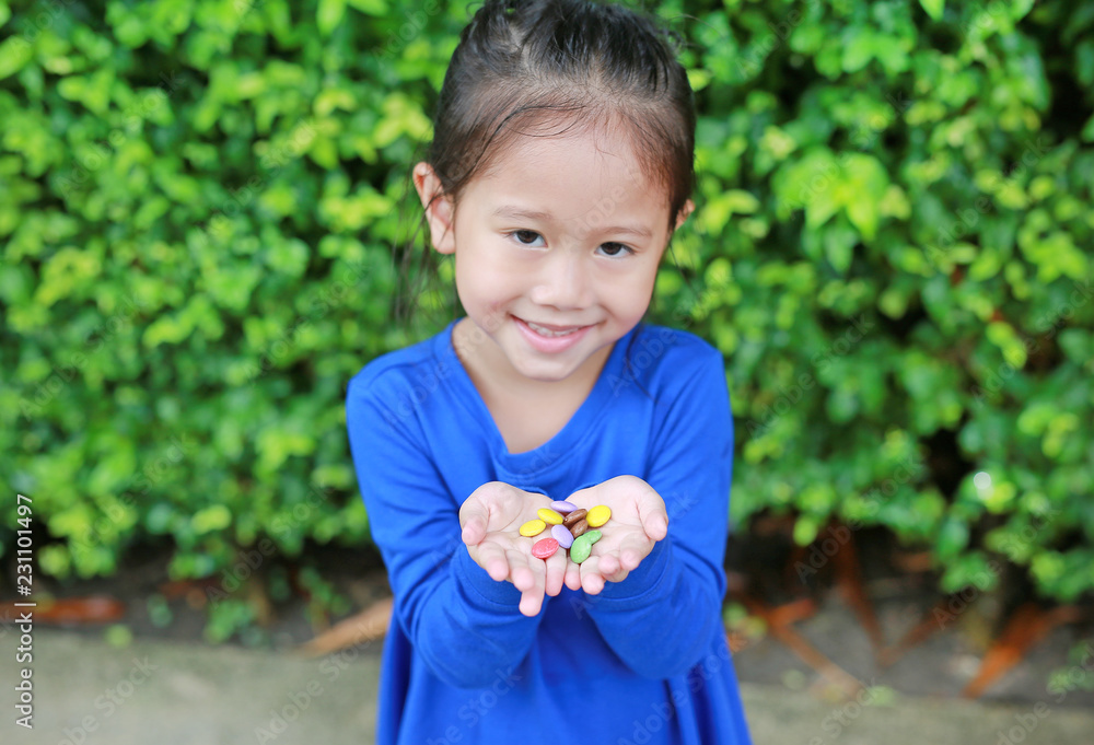 Close-up little Asian child girl holding color coated chocolate candy in her hands. Close-up little Asian child girl holding color coated chocolate candy in her hands.