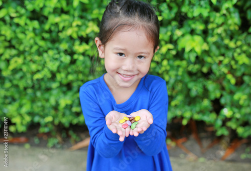 Close-up little Asian child girl holding color coated chocolate candy in her hands.