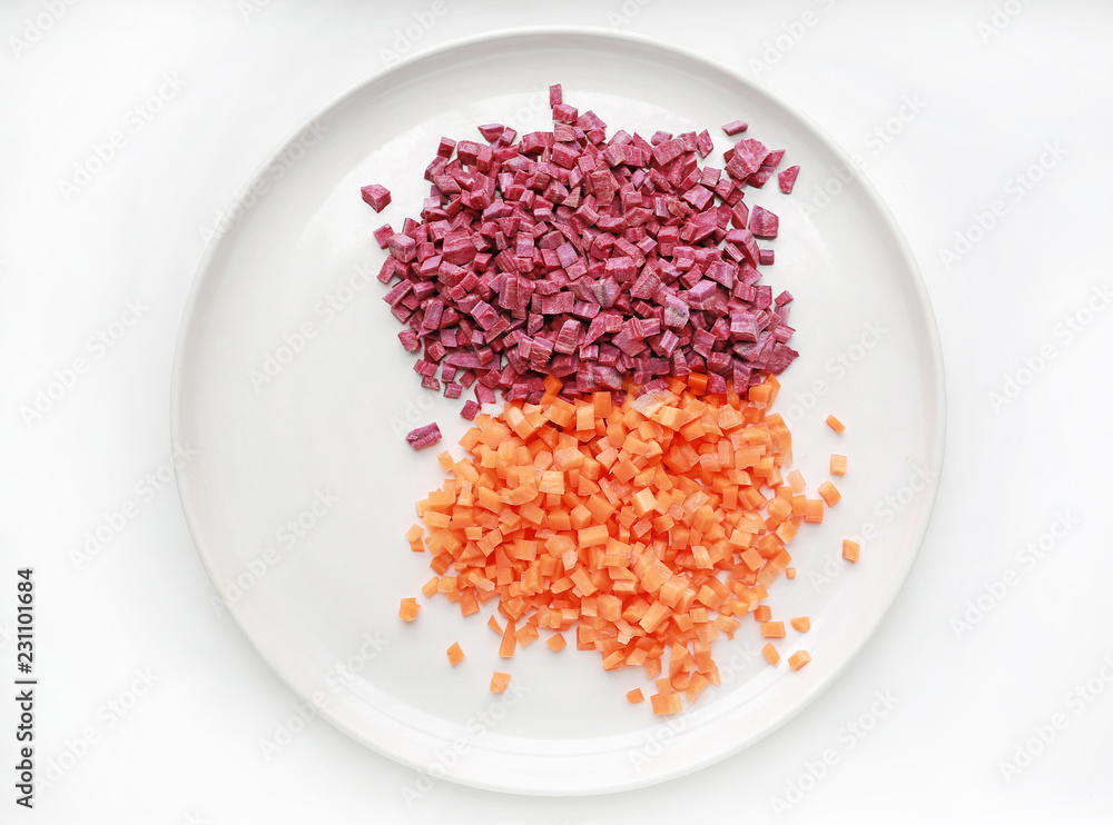 Chopped sweet purple potatoes and carrot on plate against white background.