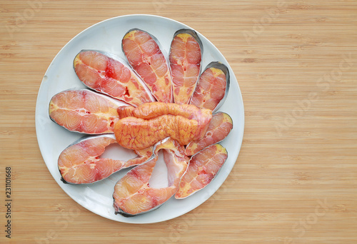 Sliced fresh Iridescent shark or Striped catfish with egg on white plate against wooden board background. photo