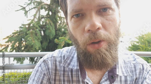 a bearded man sitting at a wooden table in a summer cafe eating French fries. photo