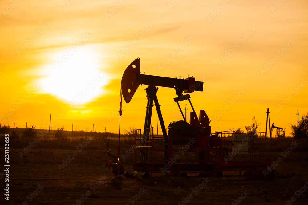 In the evening, the outline. The oil pump, industrial equipment. Field site, oil pumps are running. Rocking machines for oil production in a private sector.