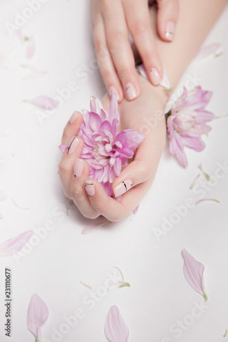 Hands of woman with nude manicure on nails and pink flowers