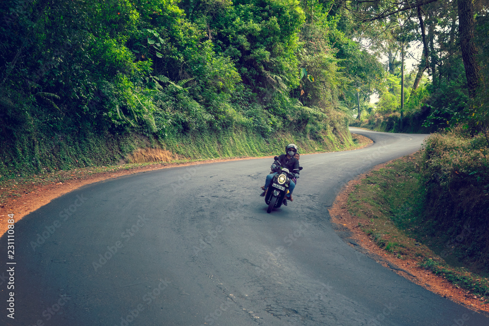 Indonesia, Ubud 5/10/2018 A motorcyclist driving along a winding road in the forest Indonesia, Ubud 5/10/2018 A motorcyclist driving along a winding road in the forest