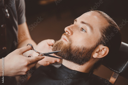 Obraz na plátně Hipster client man visiting in barber shop shaving beard scissors