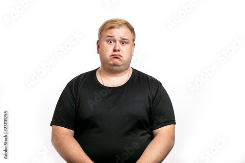 Stressed overweight plump male having sad expression wearing black T-shirt curving his lip knowing sad news. Bemused fatty guy isolated over white background. People and negative emotions.