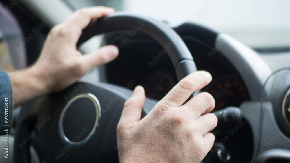 Male hands on steering wheel inside car, selected focus