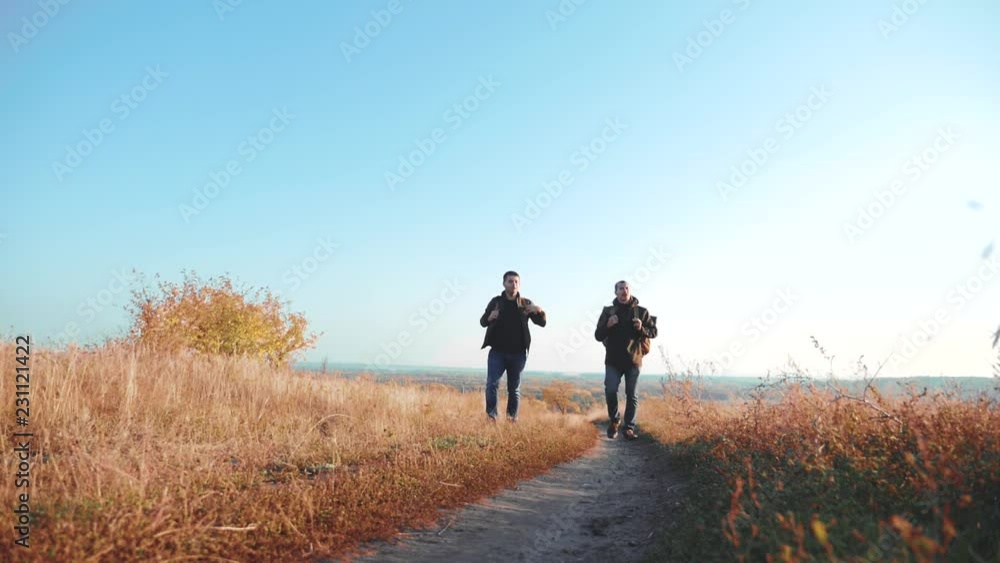 Two men road path traveler hiking with backpacks are walking along the path climbing into the mountains. slow motion video. Tourist Hipster Hiker traveler on background view blue sky clouds go hiking Two men road path traveler hiking with backpacks are walking along the path climbing into the mountains. slow motion video. Tourist Hipster Hiker traveler on background view blue sky clouds go hiking