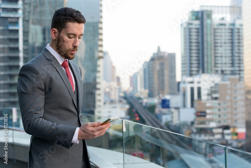 Young handsome Caucasian businessman using mobile phone at rooft photo