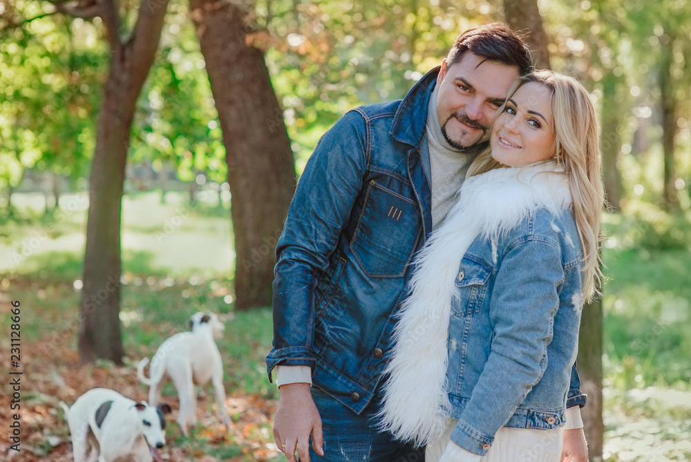 beautiful lovely young couple (woman and man) in jeans clothes walking with two whippet dogs outdoor in autumn (fall) - healthy lifestyle. Pets, love and friendship concept
