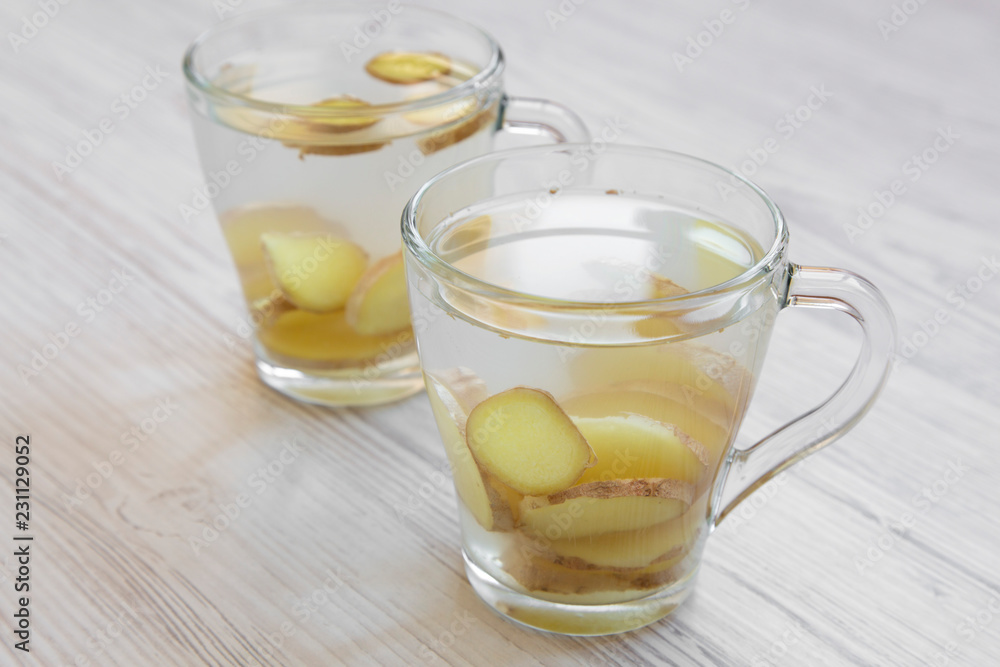 Two mugs of homemade ginger tea with lemon on white wooden surface, side view. Close-up. Two mugs of homemade ginger tea with lemon on white wooden surface, side view. Close-up.