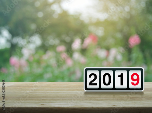 Retro flip clock with 2019 text on wooden table over blur pink flower and tree in park, Happy new year 2019 concept