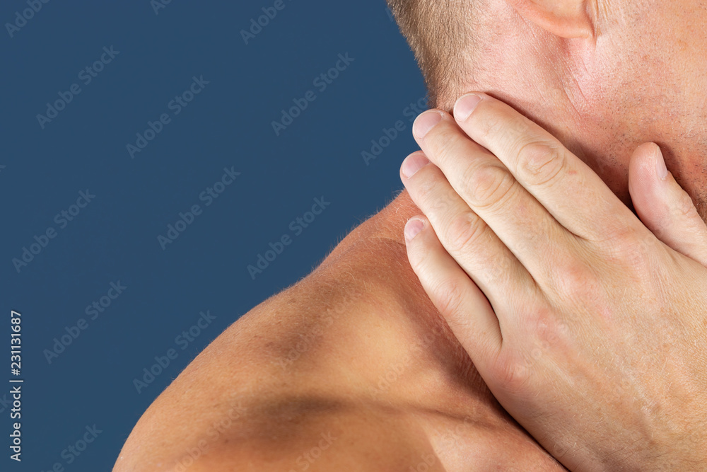 Man holding his neck in pain, isolated on blue background. Lower neck pain. Shirtless man touching his neck for the pain